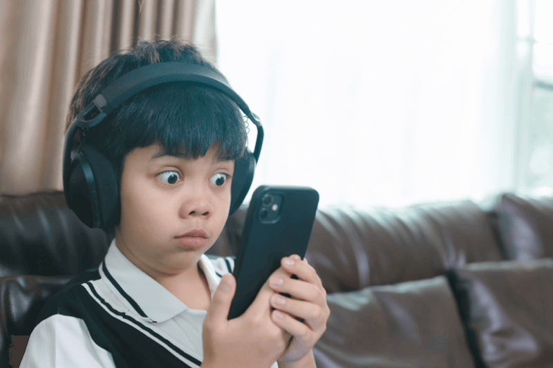 Asian boy with headphones looking shocked at smartphone screen,