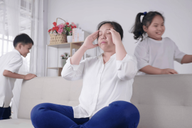 Kids tired and running near upset mother sitting at couch.