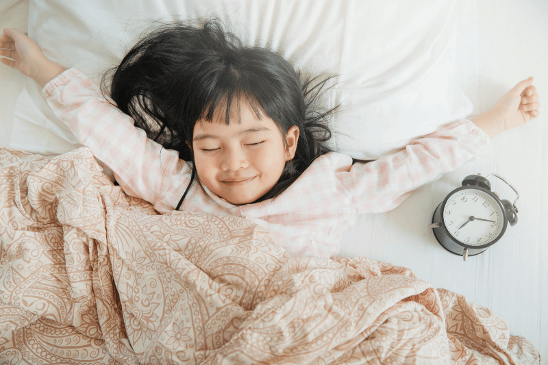 irl wakes up in morning in bed and stretches by window.