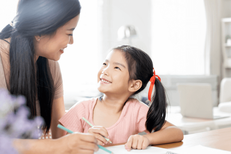 other and her small daughter sitting in cozy living room, teaching girl paint use album and colourful pencils