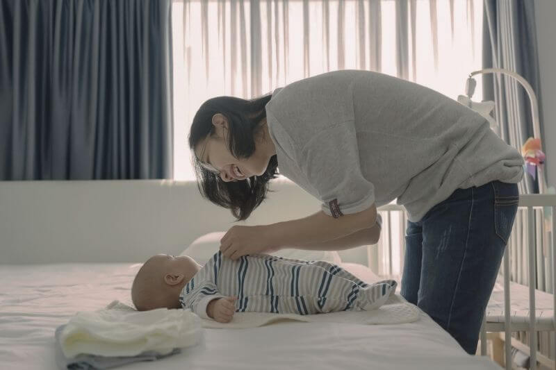 mother bonding with little infant on the bed changing diapers enjoying motherhood