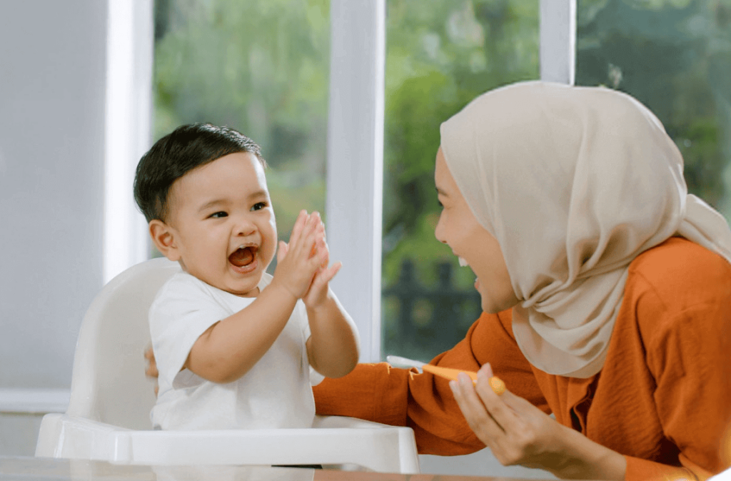 woman in orange shirt feeding little child sitting on baby chair