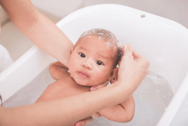 infant young boy in baby bath tub being showered by mother