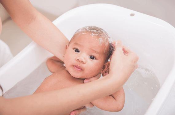 infant young boy in baby bath tub being showered by mother