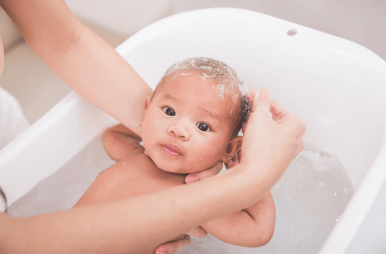 infant young boy in baby bath tub being showered by mother