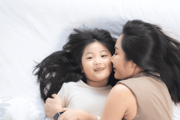 joyful mother and daughter laughing together while lying on a bed