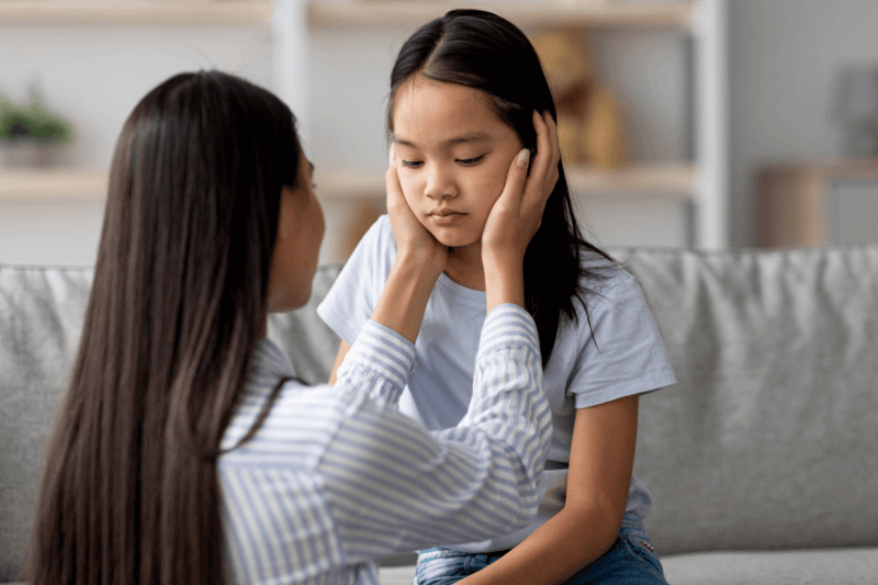 Young asian mother calming down her offended daughter after quarrel, free space
