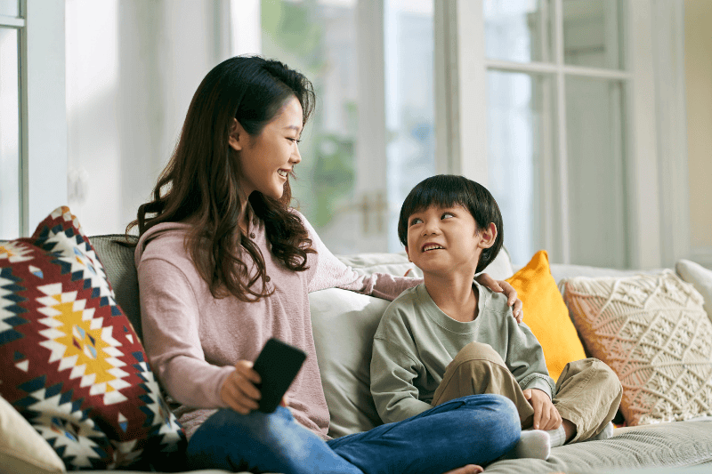 young asian mother sitting on family couch at home having a pleasant conversation with five-year-old son