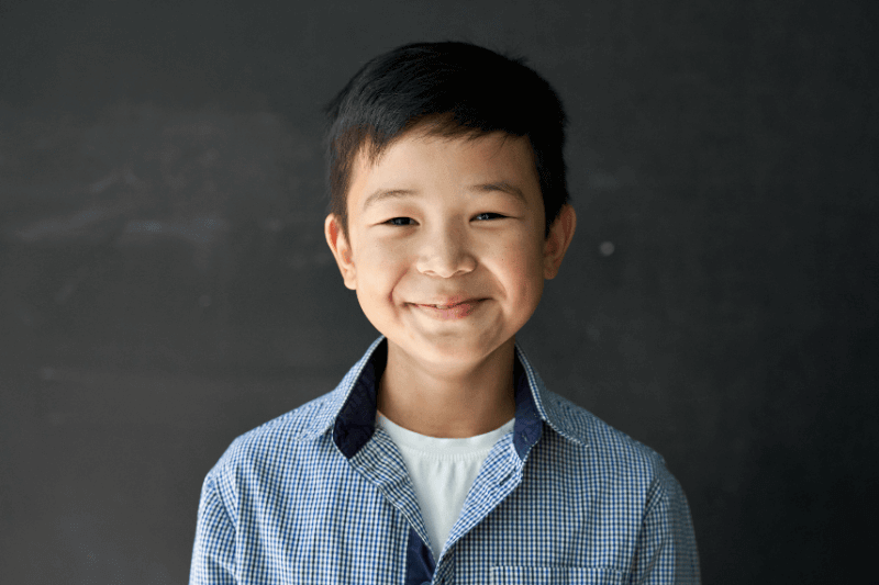 Happy cute Asian kid boy school student looking at camera at blackboard background