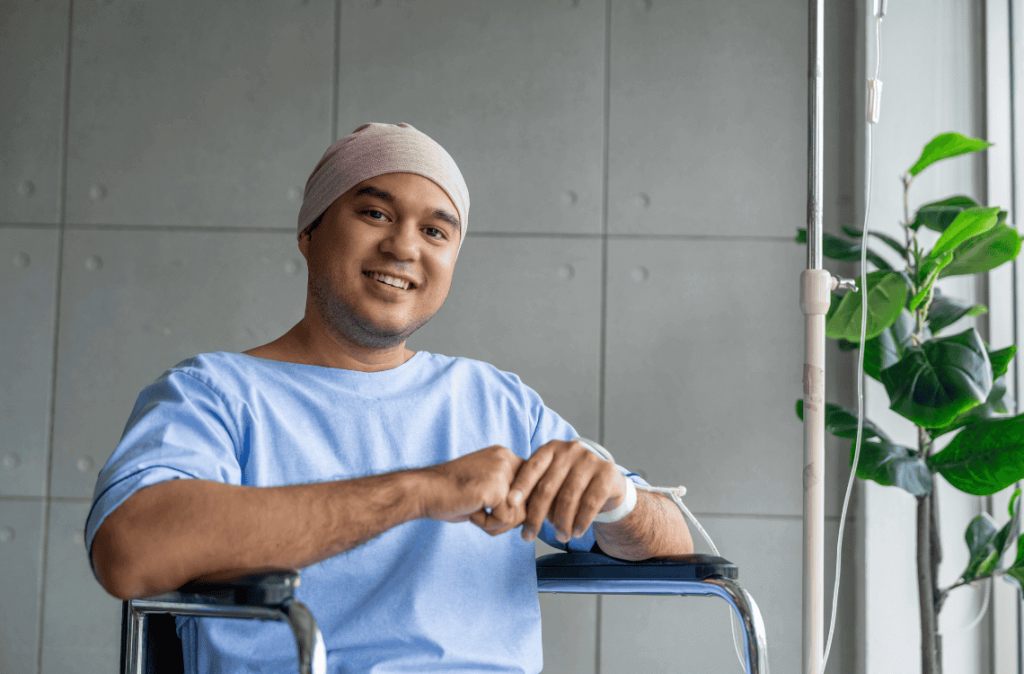 A male cancer patient in a wheelchair with an IV smiles with joy and hope showing strength and positivity during treatment