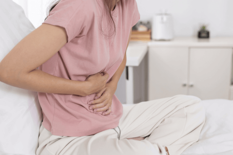 women suffering from abdominal pain while sitting on bed, concept of stomach ache, digestion issue