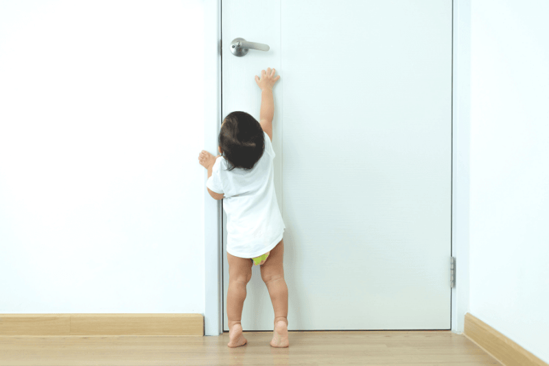 1 year old toddler Asian baby boy standing on tiptoes reaching up try to open door knob