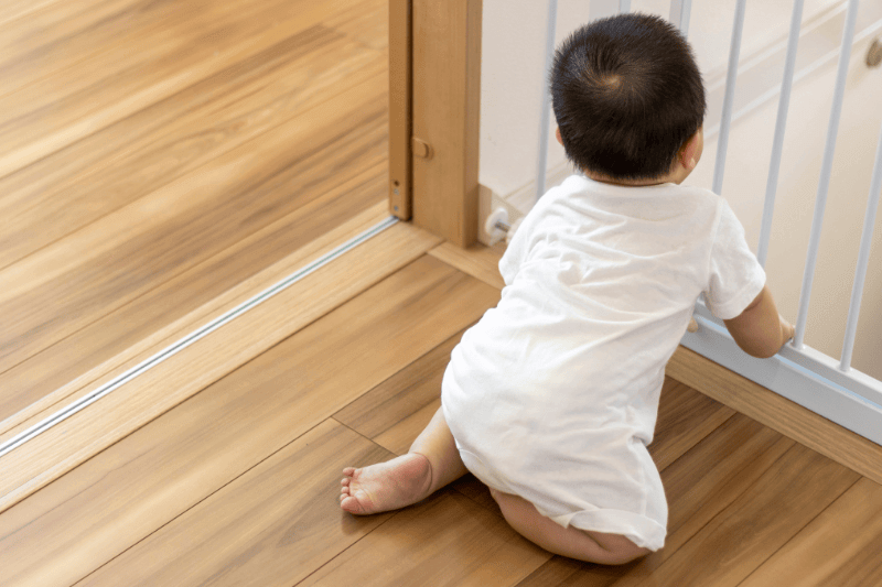 Baby's back view and baby gate, image of young child trying to open the baby gate