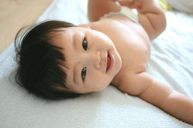 baby looking to the camera smilng and trying to roll for tummy time