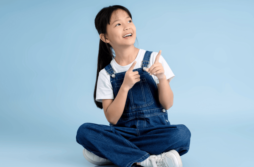 girl sitting on isolated blue background pointing at her right