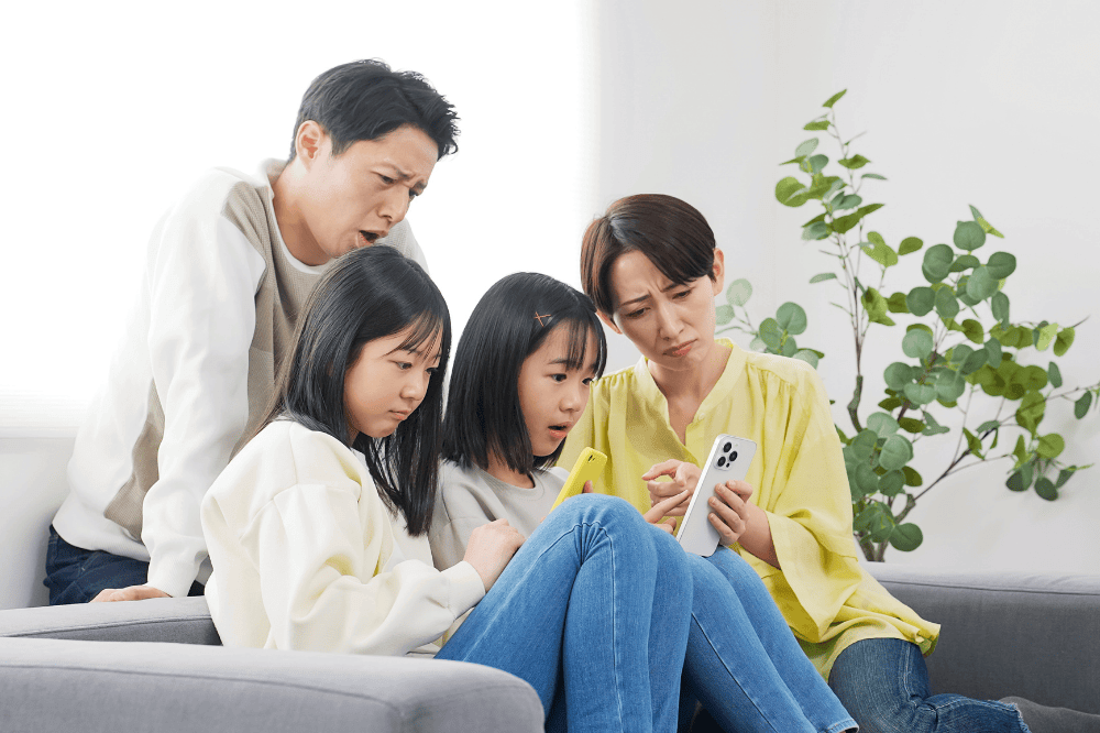 A family of elementary school girls with troubled expressions while looking at their smartphones