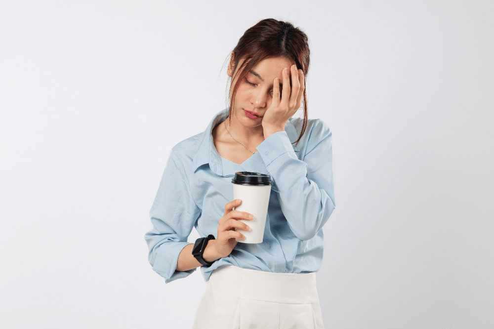 Sleep hits hard, woman yawns, hides part of face with palm, clutching coffee, showing tired eyes falling asleep, sleepy stress, and weight of another sleep-deprived morning. isolated white background