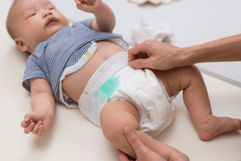 Mother changing baby diaper on table at home
