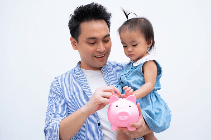 Dad teaching his daughter to save money, girl putting coins into piggy bank