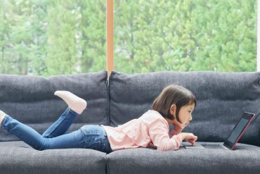 girl lying on sofa facing laptop screen