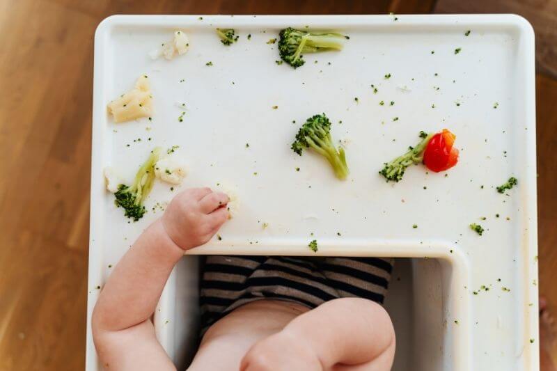 Feeding. Baby's first solid food. Baby boy eating vegetables. Child eating broccoli at home. Smiling beautiful baby curiously trying different vegetables.