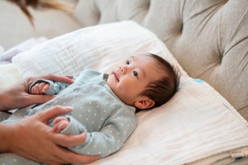 An adorable, innocent Asian newborn baby son in blue pajamas is in his bed, talking and playing with his mom. infant, toddler, child
