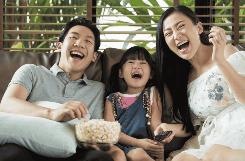 Happy Asian family spending time by watching tv together on sofa in living room. family and home concept