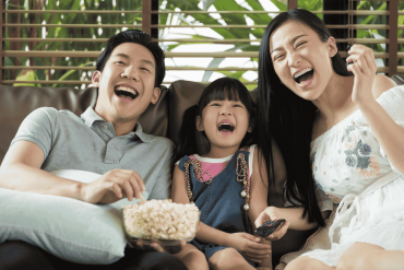 Happy Asian family spending time by watching tv together on sofa in living room. family and home concept