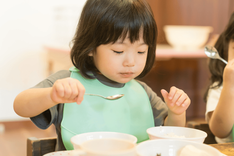 young asian toddler eating healthy balanced meal self feeding