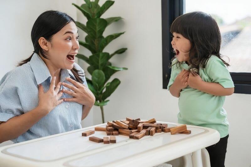 toddler girl with her mother playing wooden block toy together and shocked with tower collapses