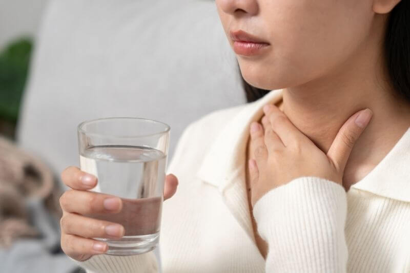woman holding glass of water having sore throat