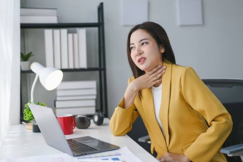 Young manager is touching her neck, feeling unwell while working at her desk in her office