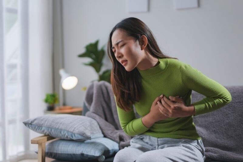 Young woman is suffering from chest pain while sitting on her living room sofa