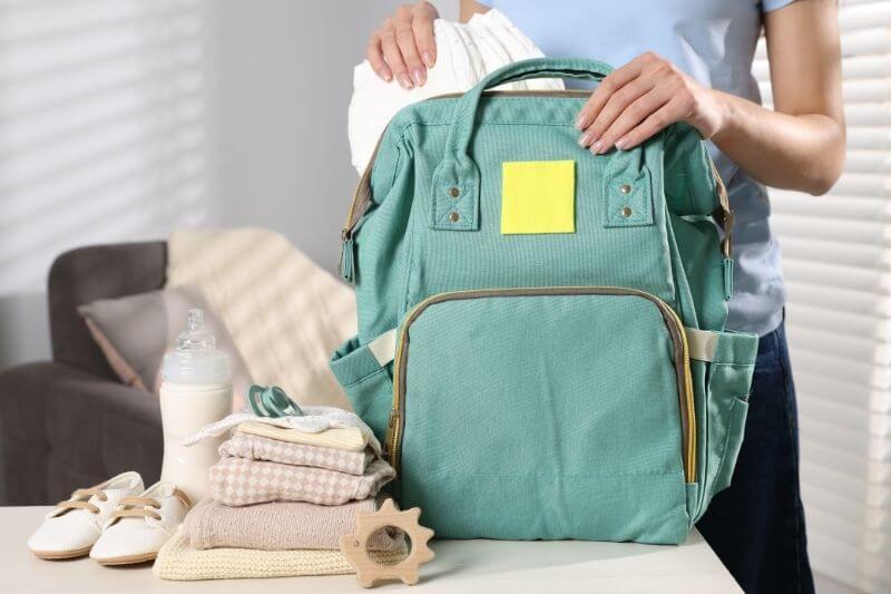 Mother packing baby's stuff into bag at white table, closeup