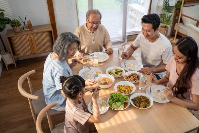 Asian Big happy family spend time have lunch on dinner table together. Little kid daughter enjoy eating foods with father, mother and grandparents. Multi-Generation relationship and activity in house