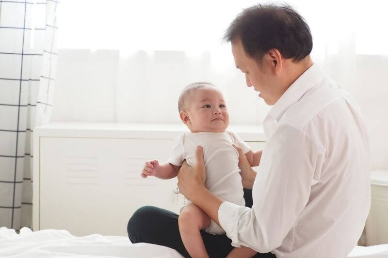 Asian father gently touching and comforting his cute newborn baby feeling unwell and crying at home Father looking after baby with love and care concept