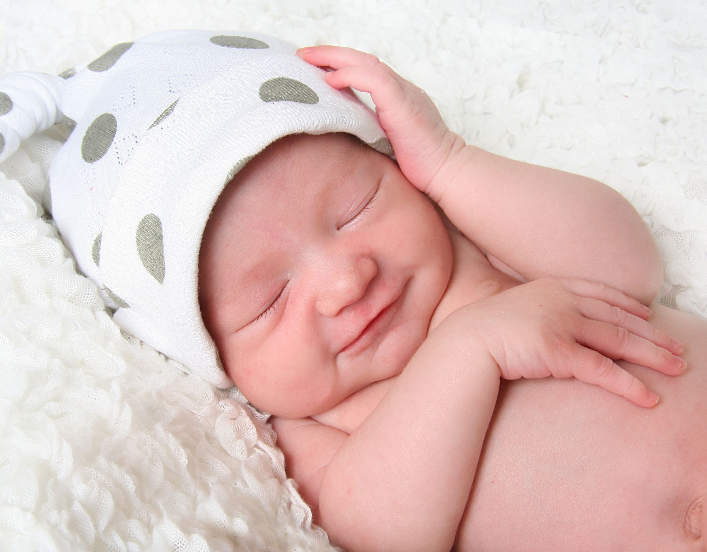 newborn baby girl sleeping wearing a polka dot hat.