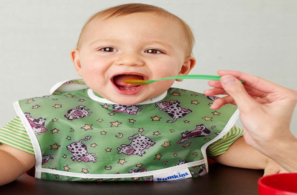 happy baby eating and wearing green bib