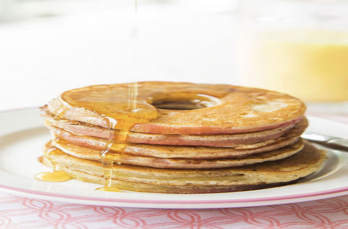 stack of apple ring pancakes on a plate drizzled with maple syrup