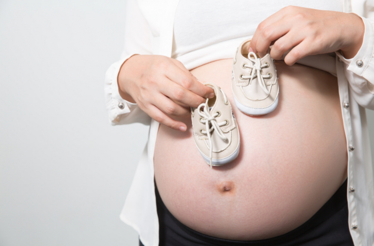 Ibu hamil memegang kasut bayi.